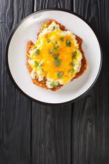 English fast food Parmo with chicken fillet breaded with bechamel sauce and cheddar cheese close-up in a plate on the table. vertical top view from above