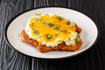 Breaded chicken Parmo baked with bechamel sauce and cheddar cheese close-up in a plate on the table. horizontal