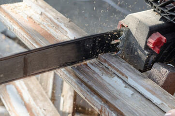 Black hand electric saw in operation. Worker sawing wood