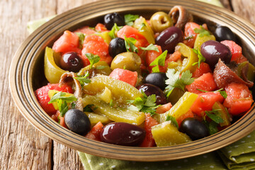 Delicious salad of tomatoes and green peppers Chlada felfel with anchovies and olives close-up in a bowl on the table. horizontal