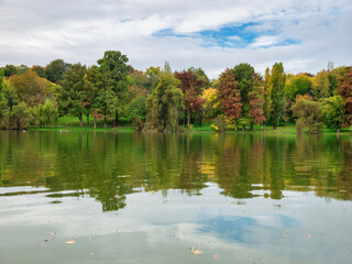 Nature landscape with colorful trees and the sky reflecting in the water of a lake. Autumn landscape.