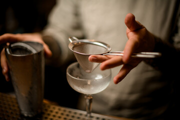 close-up on hand of bartender in which he holds sieve over wine glass
