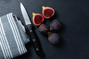 Still life of black figs with a knife and a cloth on a slate base. Three whole figs and one split