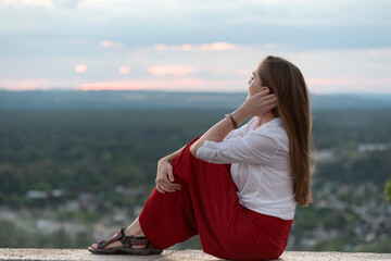 Beautiful woman sits on panoramic platform and touches her hair with her hand. Portrait of stylish woman