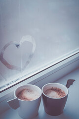 Two cups of coffee by the window. Cups of an angel and a demon. - 392592377