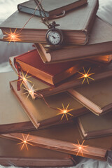 A stack of old books with Christmas garland. Pocket watch on a chain. - 392592522