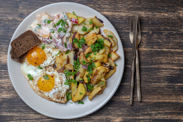 Ukrainian food, fried potatoes with onions, eggs, vegetable salad, black bread on wooden background