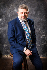 Fototapeta na wymiar Mature businessman in a suit sitting on chair studio portrait.