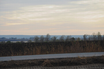 The landscape is a road, a mown black field against the background of a blue sky, trees and a lake in the distance.