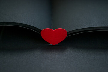 Red heart on an open notebook. Matte black sheets. - 392594995