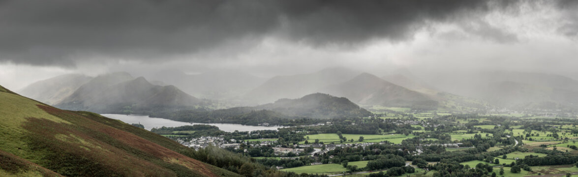 Stunning epic landscape image across Derwentwater valley with falling rain drifting across the mountains causing pokcets of light and dark across the countryside