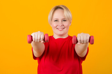 beautiful young plump female in a red t-shirt with dumbbells on a yellow background