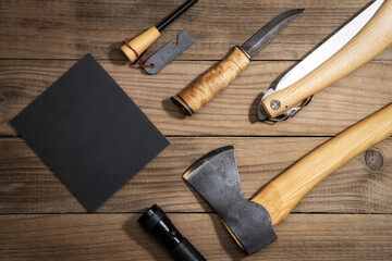 Hiking equipment on wooden surface. Flat lay of outdoor travel items. Axe, saw, flashlight and knife. Copy space.
