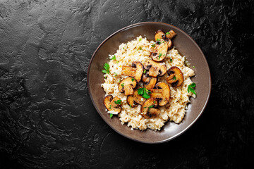 Risotto with brown champignon mushrooms on black stone background. top view