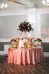 Festive candy bar with cake, macaroons, desserts and fruit decorated with flowers on a round table
