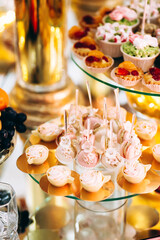 Festive candy bar with cake, macaroons, desserts and fruit decorated with flowers on a round table