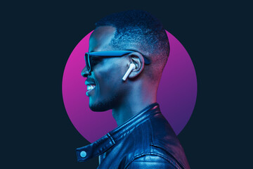 Neon portrait of smiling african american man listening music with earphones, wearing black leather...