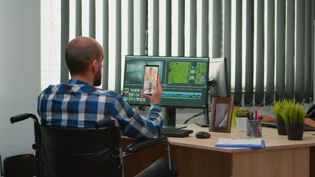 Handicapped videographer in wheelchair talking on webcam with cowerkers while editing a video project creating content in modern company office. Creator blogger working from photo studio.