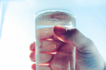 Glass with water in hand. Water in a glass against the blue sky.