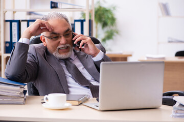 Old male employee using phone in the office