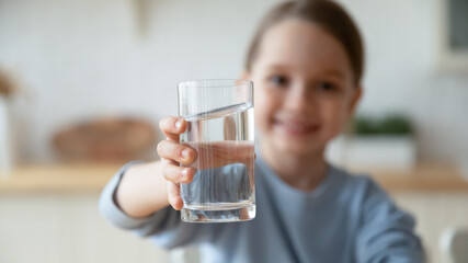 Close up smiling little girl holding glass of pure mineral water, offering to camera, cute pretty...