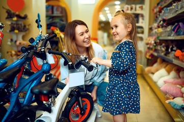 Fototapeta na wymiar Mom and little girl choosing bicycle, kid's store