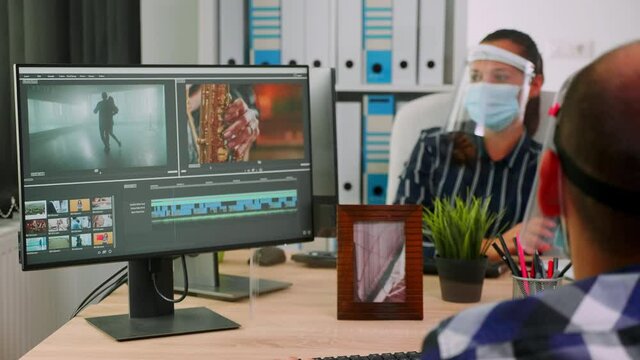 Paralysed man videographer with face mask editing video project creating content sitting in wheelchair in new normal office. Bloggers working durig global pandemic respecting social distance.