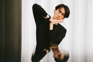 Young asian handsome man look in front of camera near white wall in black hoodie with watch on his hand 