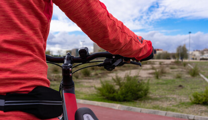 A person with an orange sweatshirt and a small fanny pack holds a bike next to them while looking at a park and a beautiful blue sky in the background