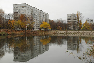 Fototapeta na wymiar Autumn city landscape. Multi-storey buildings and trees with yellow leaves reflected in the water.