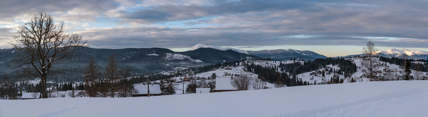 Small alpine village and winter snowy mountains in first sunrise sunlight around, Voronenko, Carpathian, Ukraine. Trace on freshly trodden path through snow drifts.