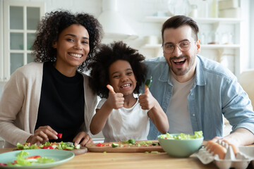 Head shot portrait happy multiracial family with kid cooking in kitchen, smiling African American...