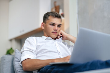 thoughtful young man browsing the Internet while lying on the couch.