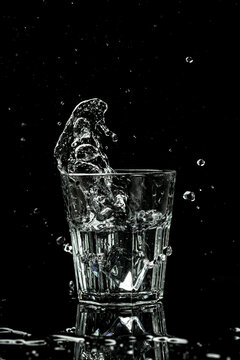 Splashes and drops of water in a glass are isolated on a black background. vertical image, place for text