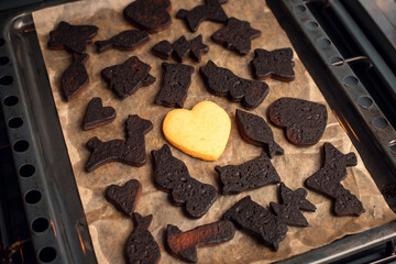 Black burned bakery with one white cookie in the middle. Christmas biscuits in different shapes on baking tray.