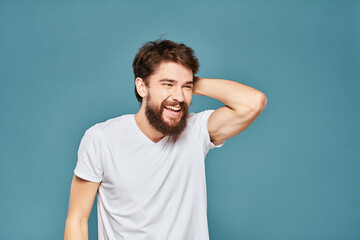 Fototapeta na wymiar A bearded man in a white T-shirt gestures with his hands emotions blue background