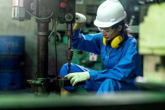 Asian Female Worker Wearing Safty Uniform And Goggle Technician Or Turner Girl Use The Screw Machine To Drill The Metal Product In The Factory Workshop Workplace.