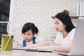 Smiling Asian mother and little girl child is drawing and Painting with wooden colored pencils on paper together in worksapce area at home. Homeschool and educational concept