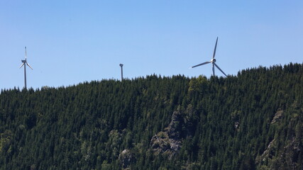 Wind turbines in a forest with rock formation in front of it.