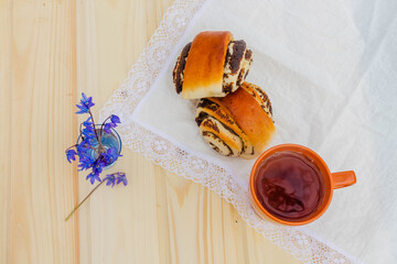 Homemade bread roll with poppy seeds and sugar, rolls on a white tablecloth. A Cup of tea and blue flowers.