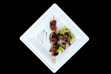 Pig kebab on a stick on a plate with green salad