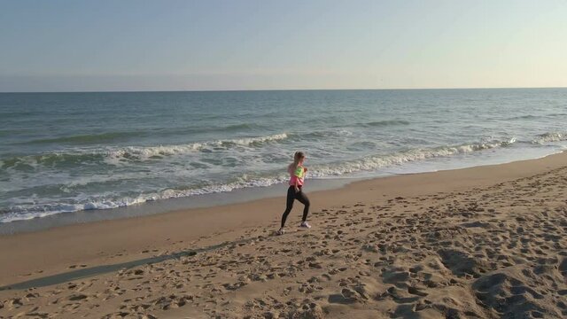 young fit woman jogging along the beach near the sea at sunset, sports, recreation, areal view of female jogger at the seaside