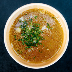 Chicken broth in a paper cup on a dark background