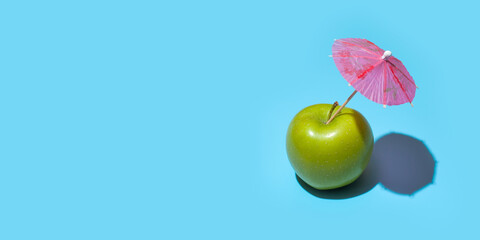 Fototapeta na wymiar Concept of fresh green apple with a umbrella isolated on blue background. Copy space. Free space for your text
