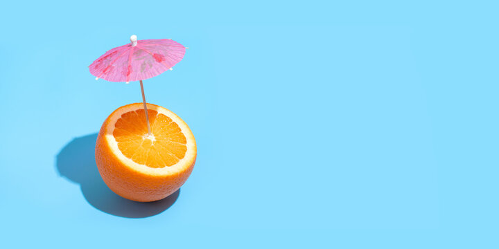 Fresh juicy orange with a cocktail umbrella isolated on blue background. Concept of Healthy eating and dieting. Drink concept. Copy space. Free space for your text