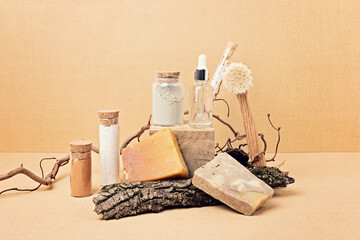 Fototapeta na wymiar Natural bristle body brush with serum, soap and clay masks displayed with pieces of wood on sand beige background. Presentation of organic eco friendly spa beauty products