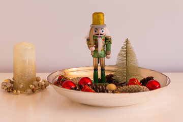 Obraz na płótnie Canvas Cute holidays interior decoration with nutcracker soldier in golden bowl with cones, tiny gift parcels, tree and balls 