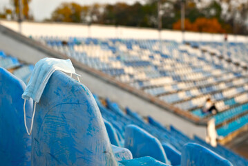 Blue protective mask on the background of chairs. The mask was left by the fan at the stadium. The concept of prohibition during a coronavirus pandemic.