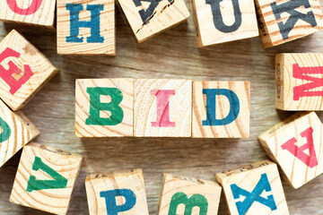Alphabet letter block in word bid with another on wood background