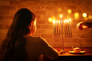 Low key image of jewish holiday Hanukkah background with girl looking at menorah (traditional candelabra) and burning candles